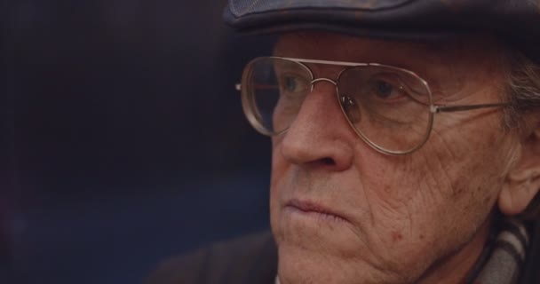 Close up of the face of senior Caucasian man pensioner in glasses and hat who sitting in the tram or bus in the evening and coming back home. — стокове відео