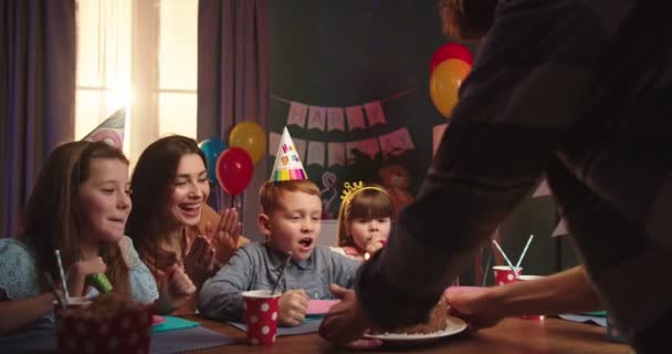 Alegre familia celebrando un cumpleaños de teh pequeño hijo lindo - niños sentados con una madre y un padre trayendo un pastel con velas, entonces el niño soplando velas . — Vídeo de stock