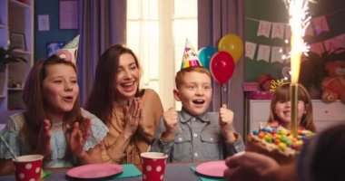 Annesi ve kız kardeşleriyle birlikte doğum günü pastasını bekleyen beyaz, şirin bir çocuk. Babam masaya koyarken tezahürat yapıyor, mumlar üflüyor..