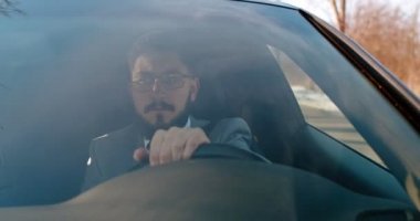 Beyaz tenli, gözlüklü, ciddi bir adam araba kullanıyor ve dikkatini çeken bir şey olarak duruyor ve yerine bir şey koyuyor. Bir terslik var..