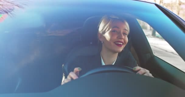 Blond caucasien jolie femme conduisant une voiture par sa rue et souriant tout en agitant la main aux gens comme saluant avec des voisins . — Video