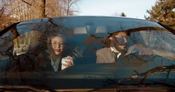 Cheerful young Caucasian couple in business style driving in a car and listening to the radio, singing while man driving and woman sipping coffee. — 비디오