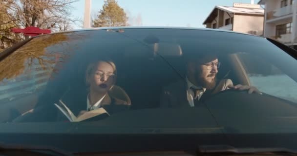Jóképű kaukázusi üzletember, aki autót vezet, miközben a női kollégája mellette ül, és ellenőriz valamit a naplójában. A munkanap tervei. — Stock videók