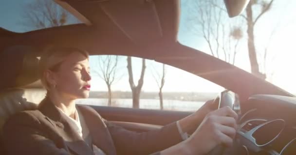 Vue latérale sur la jeune femme d'affaires blonde attrayante du Caucase conduisant une belle voiture par une journée ensoleillée le matin . — Video