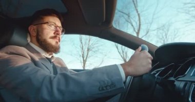 Beyaz tenli, gözlüklü, iyi görünümlü bir iş adamı güzel bir araba kullanıyor ve radyo dinliyor..