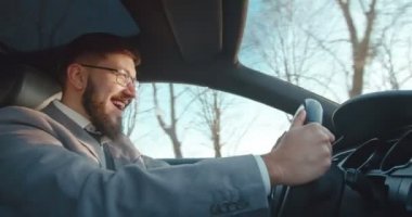 Güneşli bir günde araba süren ve gülümseyen iş stili güzel görünümlü neşeli beyaz bir adam. Yan görünüm.