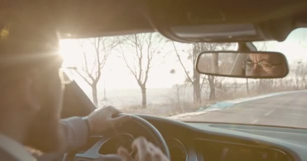 Close up da parte de trás do motorista masculino caucasiano em óculos dirigindo um carro caro agradável e refletindo em um espelho. Vista sobre o ombro . — Vídeo de Stock