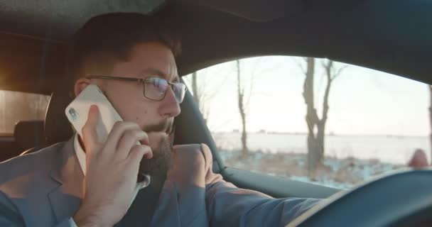 Kaukasischer junger Fahrer, Geschäftsmann mit Brille und Krawatte, der am Telefon telefoniert, während er Auto fährt und irgendwohin rauscht. — Stockvideo