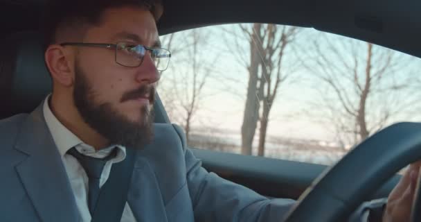 Nahaufnahme des kaukasischen jungen gutaussehenden Mannes mit Brille und Krawatte, der Auto fährt und mit einer Musik singt, die er im Radio hört. — Stockvideo