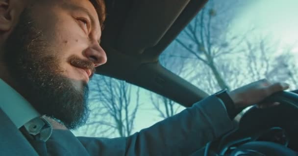 Close up of the side view of the Caucasian man with a beard and in the suit driving a car and smiling cherfully. — 비디오