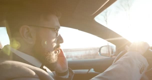 Zblízka boční pohled na bělošského podnikatele v brýlích, jak mluví na mobilním telefonu a řídí auto. Boční pohled. — Stock video