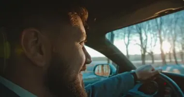 Sakallı ve araba sürerken yüzünde gülümseme olan beyaz erkek sürücünün yüzünü kapat. Yan görüş. Sonbahar sonu..