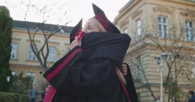 İki melez genç kız arkadaş, mezun öğrenciler kucaklaşıyorlar, neşeyle gülüyorlar ve birbirlerini mezuniyetten sonra kutluyorlar. Dışarıda..