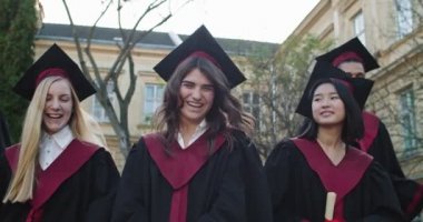 Çok ırklı genç kızlar üniversitenin mezuniyet töreninde şapkalar ve cübbeler içinde gülüyor ve eğleniyorlar..
