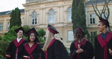 Genç melez ırklar, neşeli kızlar ve erkekler mezuniyet töreninde diploma aldıktan sonra keyifle yürüyen ve eğlenen mezun öğrenciler..