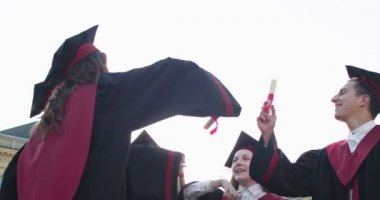 Aşağıdan akademik şapkalar ve cübbeler içinde mezun olan genç erkek ve bayanların el ele tutuşup diploma ve sertifikalarını bir araya getirmelerine bakın. Evet, biz yaptık..