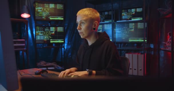 Caucasian woman hacker with blond short hair sitting in dark room with monitors at desk and typing on keyboard of computer. Female hacking online system. Stealing information concept. — Stock Video