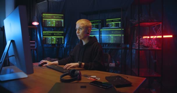 Caucasian woman with short blond hair working in cyber security center and analyzing data. Female hacker typing on keyboard at big computer in dark monitoring room. — Stock Video