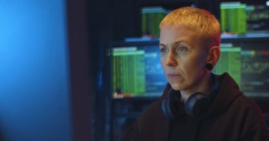 Bilgisayarda çalışan ve antivirüs kodlama programında çalışan kısa sarı saçlı ciddi bir kadın. İnternetten bilgi çalan kadın hacker. Kodları kırarken güvenli internet sistemi hackleniyor.