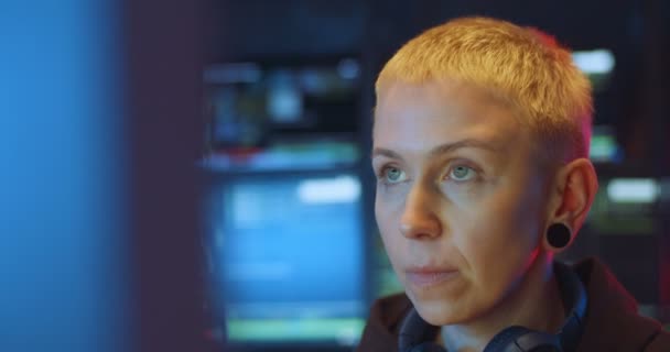 Κοντινό πλάνο της λευκής χάκερ με ξανθά κοντά μαλλιά που κάθεται σε σκοτεινό δωμάτιο με οθόνες στο γραφείο και εργάζεται στον υπολογιστή. Γυναίκα hacking online σύστημα. Έννοια της κλοπής πληροφοριών. — Αρχείο Βίντεο