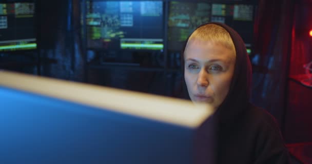 Kapüşonlu beyaz kadın hacker bütün gece ofiste monitörlerle oturup bilgisayar başında çalışıyor. Çevrimiçi kaynaklardan bilgi çalan kadın internet virüsü yayıyor.. — Stok video