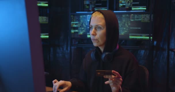 Радісна кавказька жінка в каптурі набирає номер кредитної картки на клавіатурі під час покупок в інтернеті на великому екрані комп'ютера в темному приміщенні вночі. Жіночий хакер купує і платить онлайн. — стокове відео