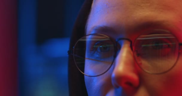 Κλείσε τα μάτια με γυαλιά Καυκάσιας γυναίκας με κουκούλα που δουλεύει στην οθόνη του υπολογιστή τη νύχτα στο γραφείο του. Γυναίκα hacker κλέβει δεδομένα στο διαδίκτυο ή τη δημιουργία και διάδοση του ιού. — Αρχείο Βίντεο