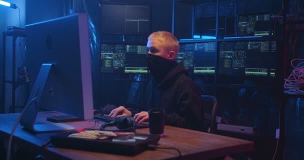 Anonymous female Caucasian hacker with masked face working on computer in front of big screen and typing on keyboard in dark room. Woman committing cyber crime. Internet data security concept. — Stock Video