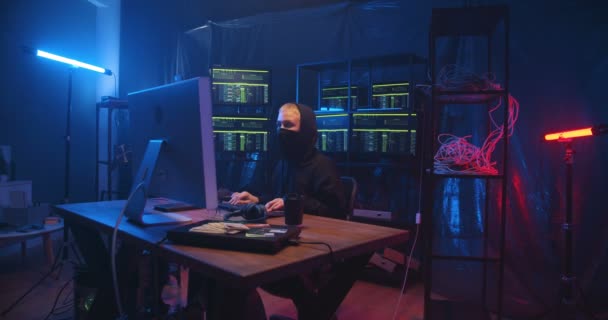 Caucasian anonymous woman with short blond hair and mask on face working in cyber security center and stealing data. Female hacker typing on keyboard at big computer in dark monitoring room. — Stock Video