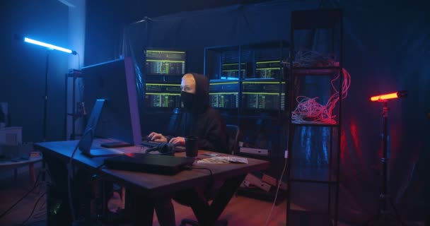 Anónimo hacker femenino caucásico escribiendo en el teclado y rompiendo el sistema seguro de la computadora en la habitación oscura con monitores. Mujer con la cara enmascarada cometiendo cibercrimen en línea y robando información . — Vídeos de Stock