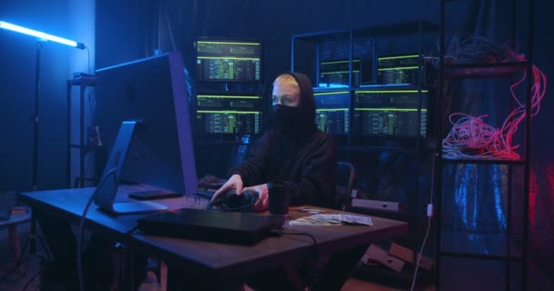 ウイルスプログラムを作成しながら、ヘッドフォンやマスクで深刻な白人女性は、コンピュータの大きな画面の前に座っている。オンラインサーバーでデータを盗む閉鎖顔を持つ女性匿名のサイバー犯罪者. — ストック動画