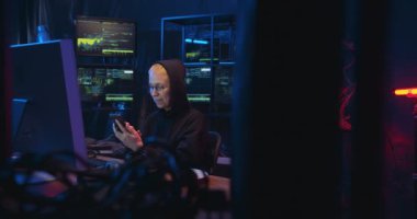 Beyaz kadın siber kadın, sarışın, kısa saçlı, siyah odada monitörlerle oturan ve akıllı telefonları dinleyen. Kadın siber polis cep telefonuyla internette geziniyor. Hacker cep telefonuna kayıyor.