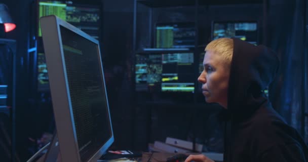 Πλευρική άποψη για Καυκάσια γυναίκα χάκερ με μαύρη κουκούλα πληκτρολογώντας στο πληκτρολόγιο και σπάζοντας το ασφαλές σύστημα του υπολογιστή στο δωμάτιο με οθόνες τη νύχτα. Γυναίκα διαπράττει ηλεκτρονικό έγκλημα στο διαδίκτυο και κλέβει πληροφορίες. — Αρχείο Βίντεο