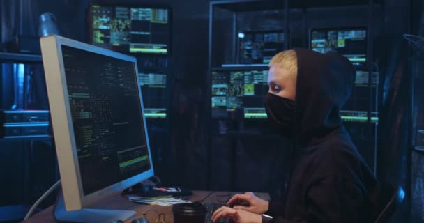 Vista lateral de la mujer hacker caucásico con la cara enmascarada de trabajo en el ordenador y la navegación por los datos en línea en la habitación oscura. Mujer cometiendo delitos ciberfinancieros. Concepto de seguridad de datos en Internet . — Vídeos de Stock