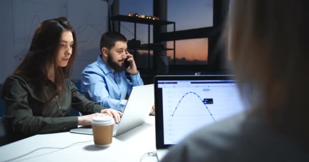 Equipo de trabajadores que trabajan hasta tarde en la noche en computadoras con gráficos, gráficos y números. Mujer bonita escribiendo y mensajes de texto en el ordenador portátil. Hombre hablando por teléfono móvil y discutiendo el problema . — Vídeo de stock