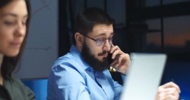 Gözlüklü, sakallı, cep telefonuyla konuşan ve akşam geç saatlerde gülümseyen beyaz tenli yakışıklı bir adam. Bulanık kadın iş arkadaşı yüzü. Erkek ofis çalışanı cep telefonuyla konuşuyor. Gece vardiyası işi.