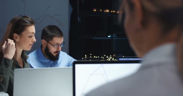 Blick über die Schulter einer Büroangestellten auf ein paar kaukasische Kollegen, die spätabends gemeinsam am Laptop arbeiten. Teamwork am Abend. — Stockvideo