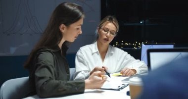 Kafkasyalı genç ve meşgul ofis çalışanları gece geç saatlerde dizüstü bilgisayarın başında belgelerle konuşup çalışıyor. Kadın iş arkadaşları proje fikirleri üzerine beyin fırtınası yapıyorlar.