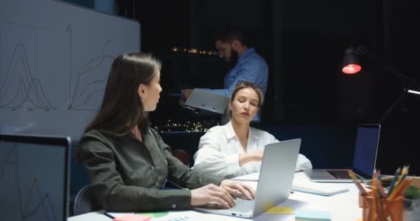 Camaradas caucásicos de buen aspecto, hombres y mujeres, teniendo una reunión de negocios en la oficina tarde en la noche. Hombre y dos mujeres trabajando con documentos y hablando por la noche . — Vídeos de Stock