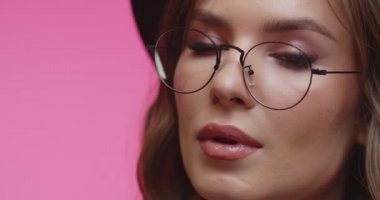 Siyah şapkalı, gözlüklü ve bakışlarını kaçıran güzel bir kadın. Pembe stüdyodaki modelin yakın çekimi..
