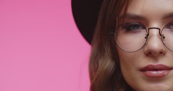 Modelo con sombrero blach y gafas mirando a la cámara. Alegre chica morena con estilo en el sombrero mirando en la cámara en el estudio con fondo rosa. Mujer mirando a la cámara en primer plano . — Vídeo de stock