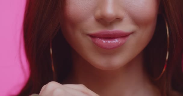 Gewas gezicht van mooie jonge vrouw met gevoelige lippen close-up op een roze achtergrond. Vrolijk stijlvol brunette meisje op zoek in de camera in de studio. Fashion shoot in roze studio met vrouw. — Stockvideo