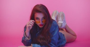 Sarı gözlüklü güzel kadın kameraya bakıyor. Pembe stüdyodaki moda kızı. Güneş gözlüklü genç bir kadın pembe arka planda kameraya bakıyor. Moda modeli.