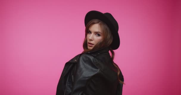 Cheerful stylish brunette girl in hat turning around and looking into the camera. Beautiful woman with long brown hair. Female looking into camera in close up with pink background. — Stock Video