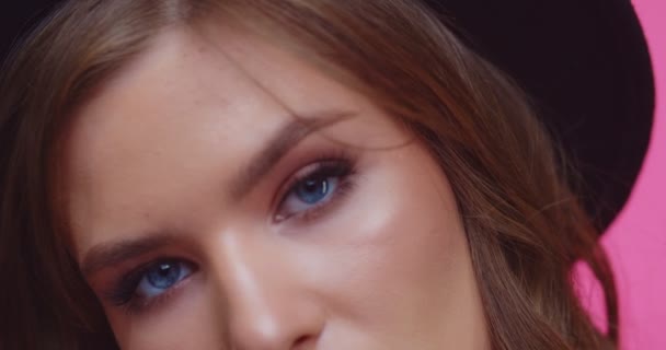 Model met blaaspet en bril kijkend naar camera. Vrolijk stijlvol brunette meisje in hoed op zoek in de camera in de studio met roze achtergrond. vrouw op zoek naar camera in close-up. — Stockvideo