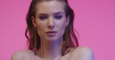 Pembe stüdyoda poz veren muhteşem bir model. Harika makyajı, zarif saç stili ve pembe arka planda zarif küpeleri olan güzel bir kadın..