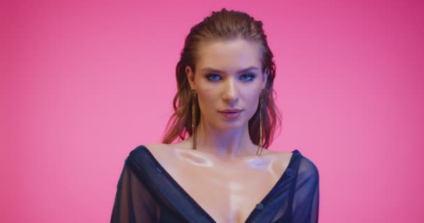 Gyönyörű modell, rózsaszín stúdióban pózol. Gyönyörű nő csodálatos smink, elegáns frizura és elegáns fülbevaló rózsaszín háttér. — Stock videók