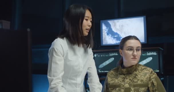 Азиатская молодая женщина показывает что-то кавказской женщине-солдату и обучает ее военно-морской стратегии управления армейским офисом. Образовательный морской военный центр для женщин . — стоковое видео