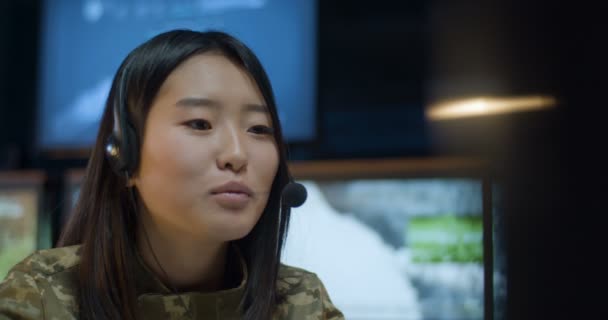 Primo piano di Asiatica giovane donna in auricolare seduto sullo schermo del computer e parlare via videochat in sala di monitoraggio nell'esercito. Soldato donna che fa chat via webcam nel centro militare . — Video Stock