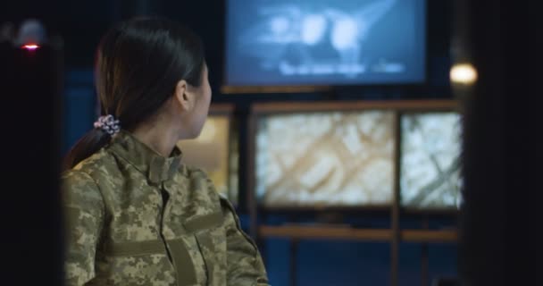 Ασιάτισσα νέα όμορφη γυναίκα με στολή καμουφλάζ που εργάζεται στο στρατιωτικό κέντρο παρακολούθησης στην οθόνη του υπολογιστή. Γυναίκα στρατιώτης στην αίθουσα ελέγχου του στρατού. — Αρχείο Βίντεο